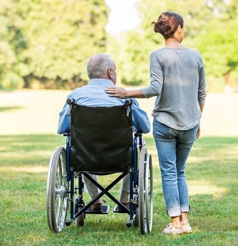 Father in a wheelchair with adult daughter overlooking green grassy area